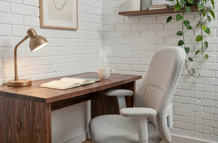 Escritório moderno e confortável em casa com mesa de nogueira, cadeira ergonômica cinza e parede de tijolos brancos pintados